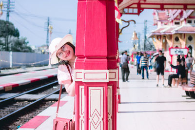 Portrait of smiling woman standing behind pillar on railroad station platform