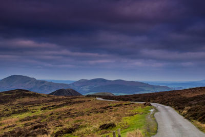 Scenic view of road amidst field against cloudy sky