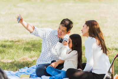 Smiling father doing selfie while sitting with family at park