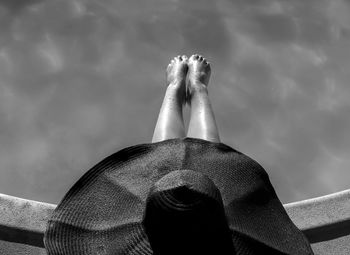 A girl with a bog black hat sitting on the edge of a swimming pool