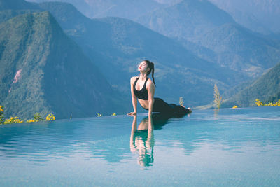 Woman meditating on infinity pool against mountains
