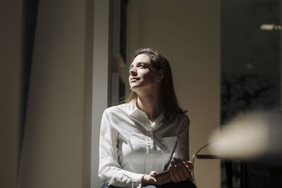 Woman looking away while sitting by window at office