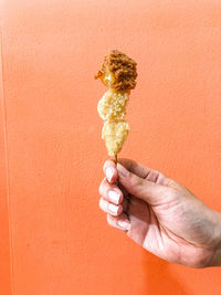 Hand holding ice cream cone against orange background