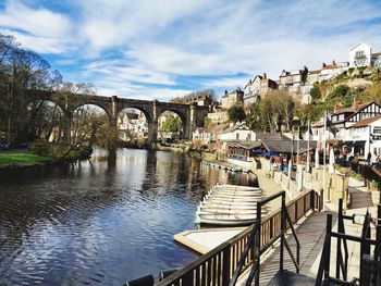 Bridge over river by buildings against sky