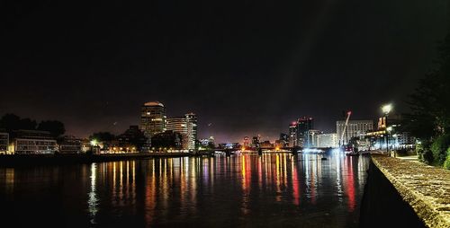 Illuminated buildings by river against sky at night