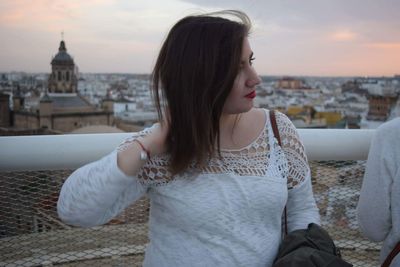 Beautiful woman in city against sky during sunset