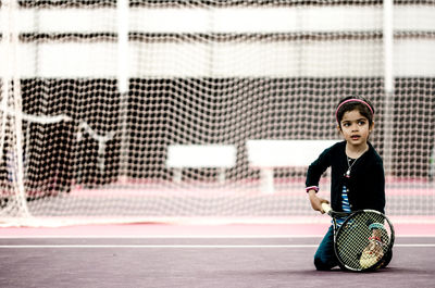 Girl looking away while kneeling in tennis court
