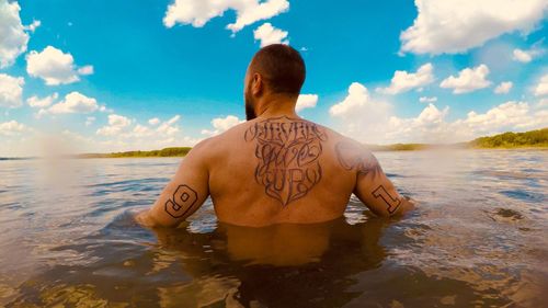 Rear view of shirtless man in sea against sky