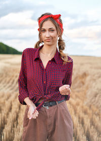 Portrait of smiling young woman standing on field against sky