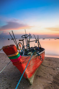 Fishing boat moored on beach against sky during sunset