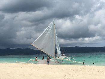 Tourists on beach against cloudy sky