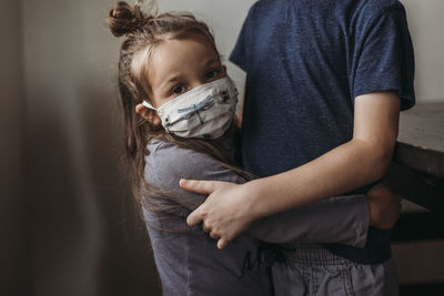 Close up of young girl with mask on being hugged by big brother negative space