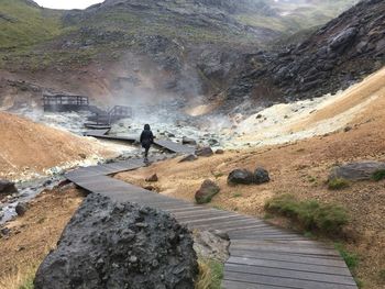 Rear view of woman walking on boardwalk by hot spring