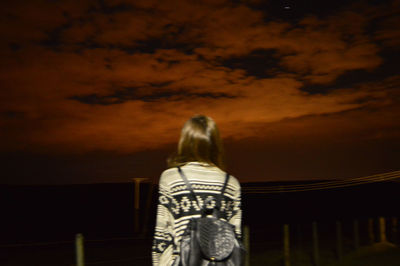 Rear view of woman standing against sky at sunset