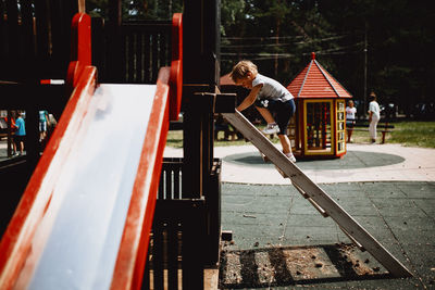 Children play in a rustic red wooden slide at the natural kids playground surrounded by pine forest.