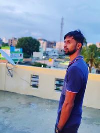 Young man looking away while standing against sky