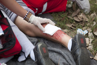 Low section of paramedic sitting by wounded woman on field