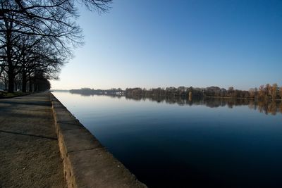 Empty footpath by river against clear blue sky