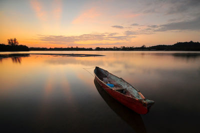 Boat moored in lake against sky during sunset