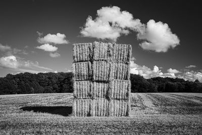 Hay bales on wooden post on field against sky