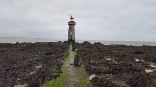 Lighthouse on beach by sea against sky