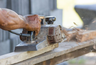 Cropped hands of carpenter using equipment on wood at workshop