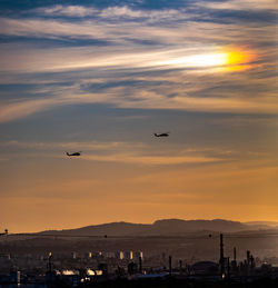 Silhouette airplane flying over sea against sky during sunset