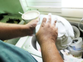 Over the shoulder view of man washing utensils in sink at home