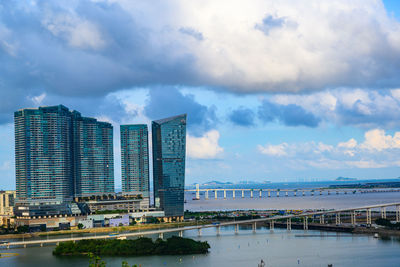 Modern buildings by river against sky in city