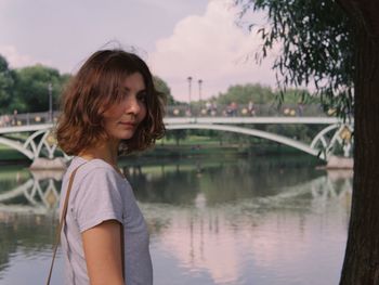 Beautiful woman looking at bridge over river against sky