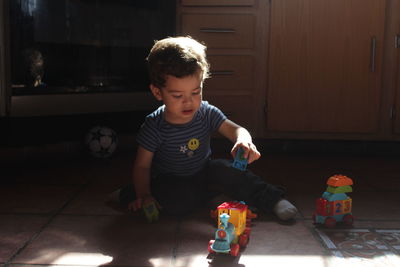 Boy playing with toy sitting on floor at home