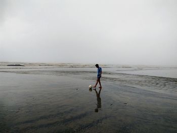 Man playing football at beach against sky