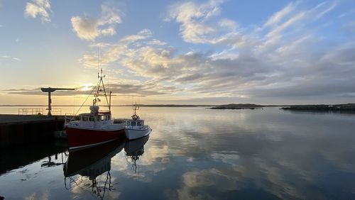 Sailboats moored on sea against sky during sunset