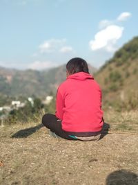 Rear view of woman sitting on rock against sky