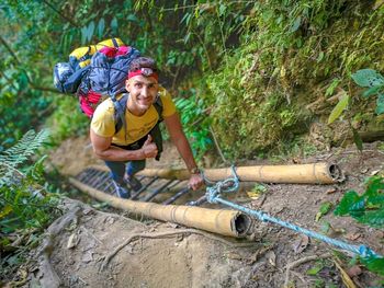 Portrait of smiling young man climbing ladder in forest