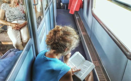 Woman reading novel in train corridor