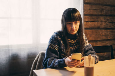 Mid adult woman using mobile phone at table in log cabin