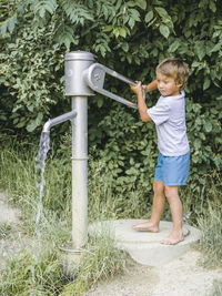 Full length of boy using water pump against plants