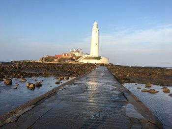 Lighthouse amidst sea and buildings against sky