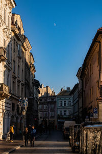 People walking on street amidst buildings in city against clear sky