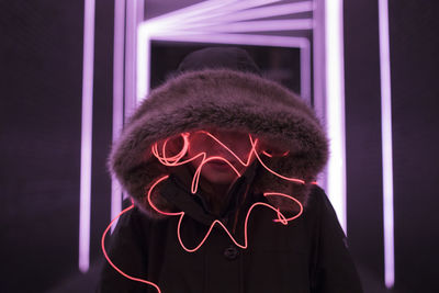 Woman in hooded clothing with light painting standing against illuminated lights