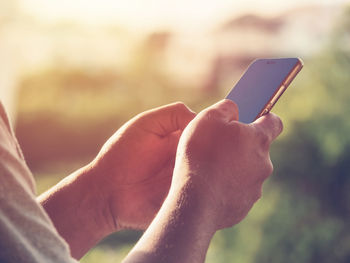 Cropped hands of man using phone during sunset