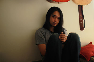 Portrait of young man sitting against wall at home