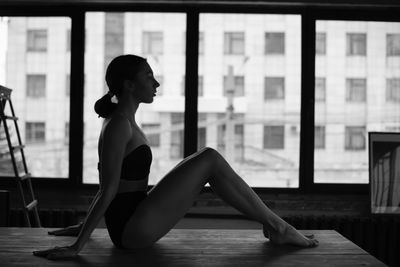 Side view of young woman sitting on window