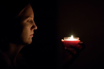 Close-up of man holding burning candle in darkroom