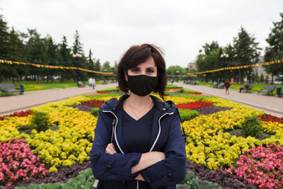 Portrait of a woman in a black protective mask on the background of a bright flower bed in the park.