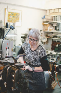 Senior woman operating machinery to make jewelry in workshop