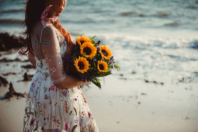 Woman with flowers standing on sea shore against sky