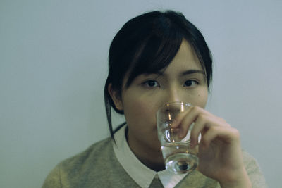 Portrait of young woman drinking water against wall
