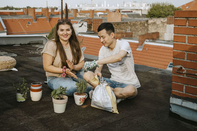 Male and female friends sitting with potted plants on rooftop